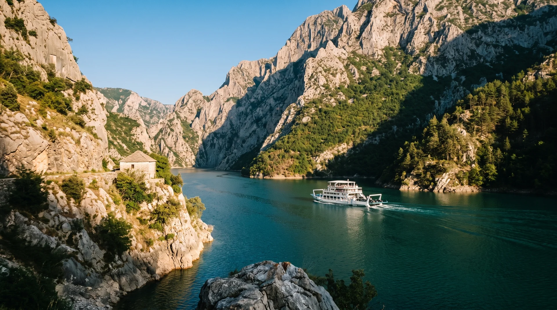 The Koman ferry threading the narrow karst gorge, green walls rising straight out of emerald water