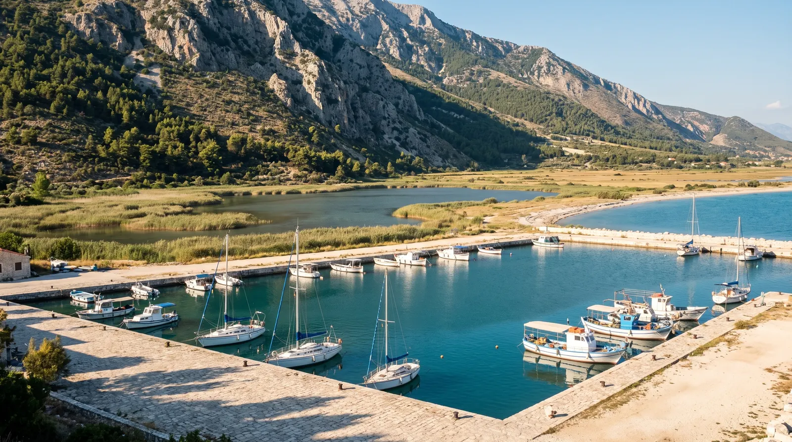 Orikum's small marina with the reed lagoon behind it and the Llogara wall beyond