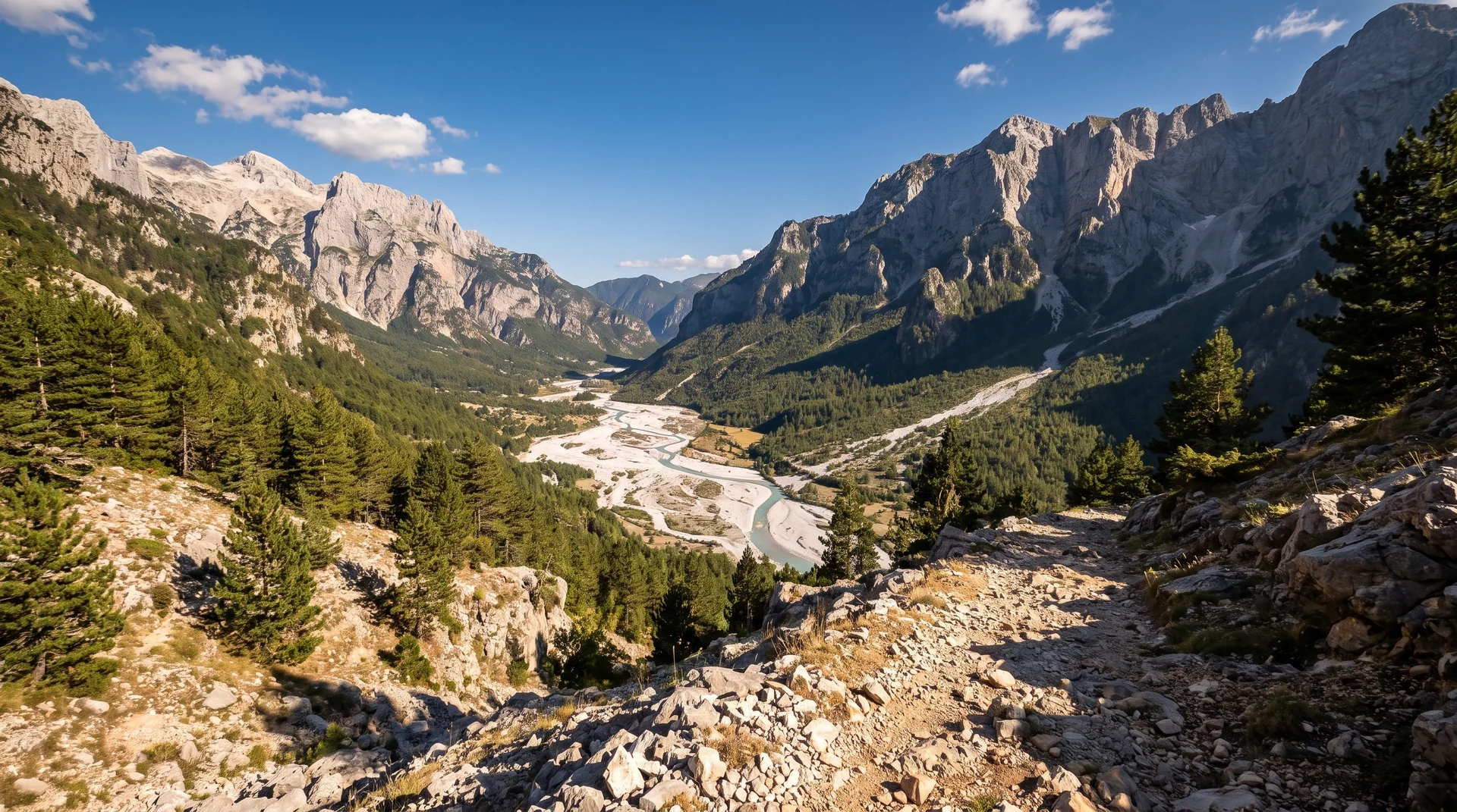 The braided white gravel bed of the Valbona river seen from the pass, with limestone peaks above